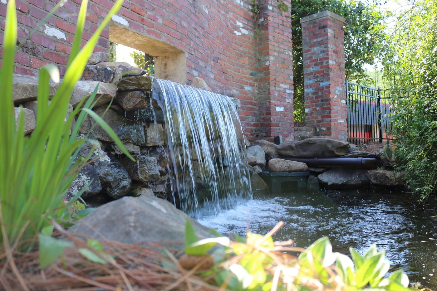 Sheer waterfall spilling from a stacked-stone wall into a planted pond
