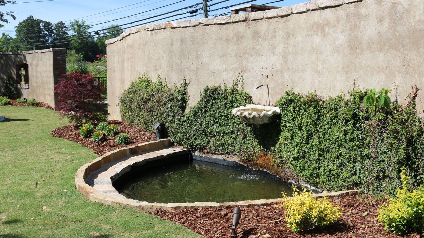 Curved stone-edged garden pond set into a lawn and planting bed