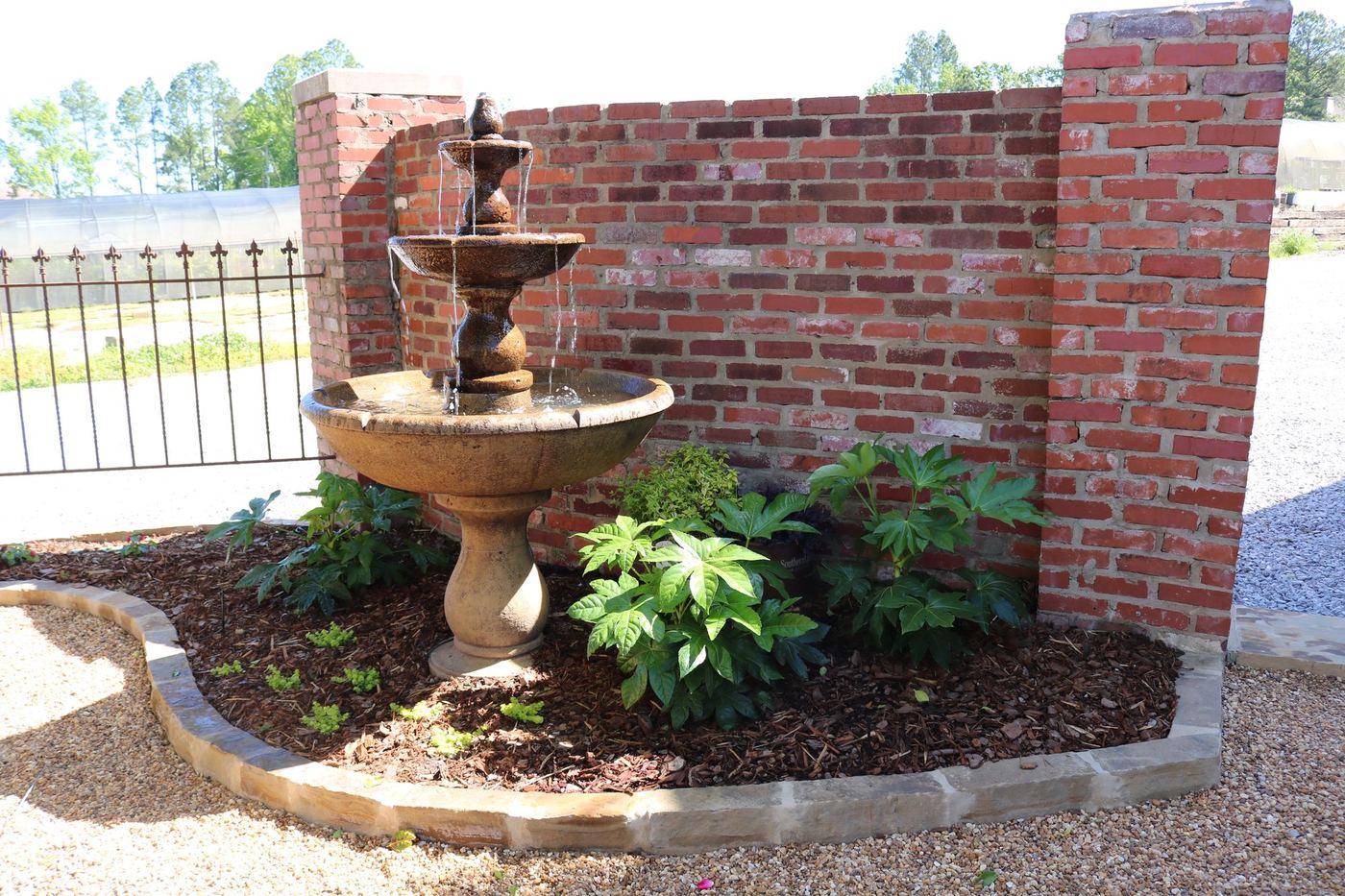 Tiered cast-stone fountain in a stone-edged planting bed against a brick wall